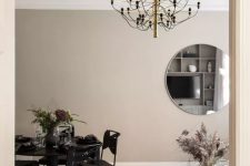 a delicate dining zone with taupe walls, a black dining set of metal and a squirky black and gold chandelier