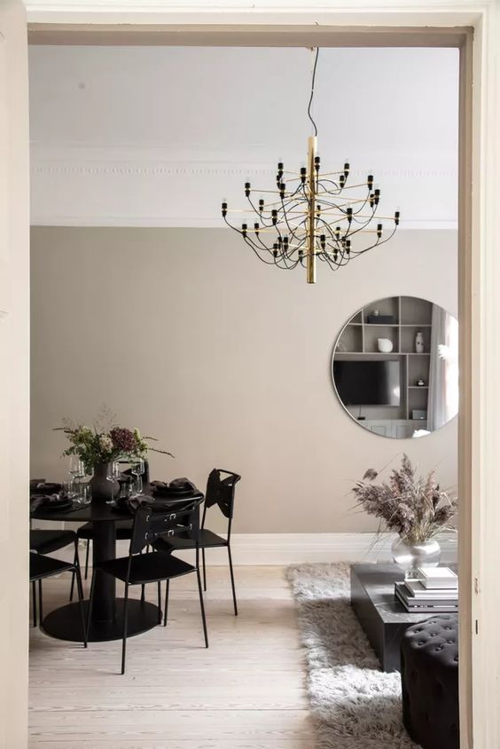 a delicate dining zone with taupe walls, a black dining set of metal and a squirky black and gold chandelier