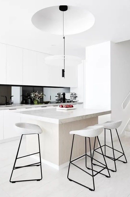 a fantastic minimalist kitchen with sleek white cabinets, white stone countertops, a black glass backsplash and black pendant lamps
