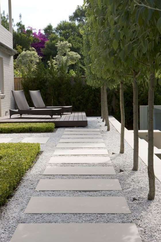 a formal outdoor space with a gravel and long paving stones plus a wooden deck and trees lining the path