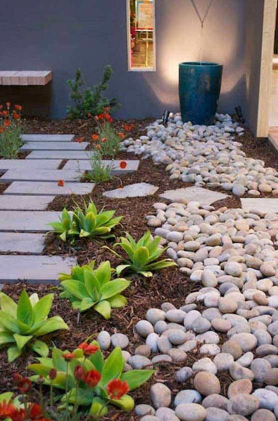 a front yard pathway of tiles lined up with succulents, blooms and large pebbles all around