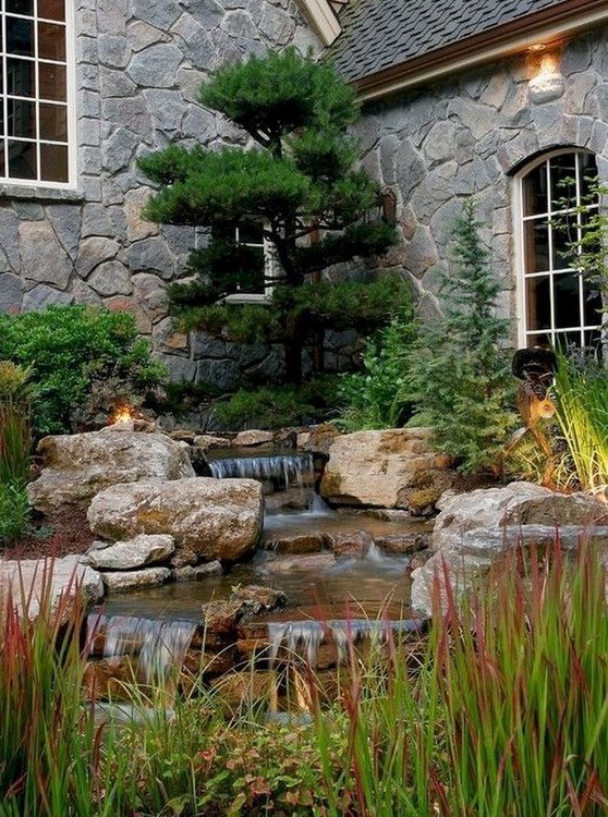 a front yard water feature with large rocks and herbs all around and a large tree over it