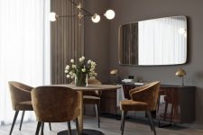 a glam and chic taupe dining room with a round table, rust-colored chairs, a glossy floating credenza and a large mirror
