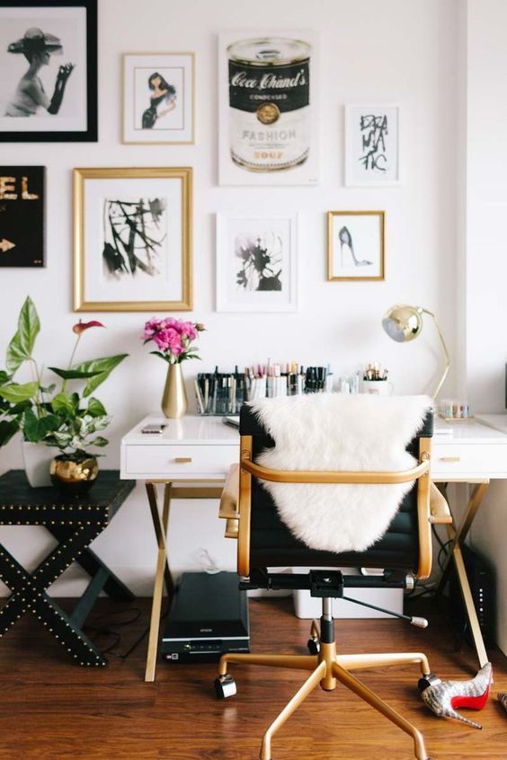 a glam home office with a chic white and gold desk, a black chair, a lovely blakc, white and gallery wall plus blooms and gold touches