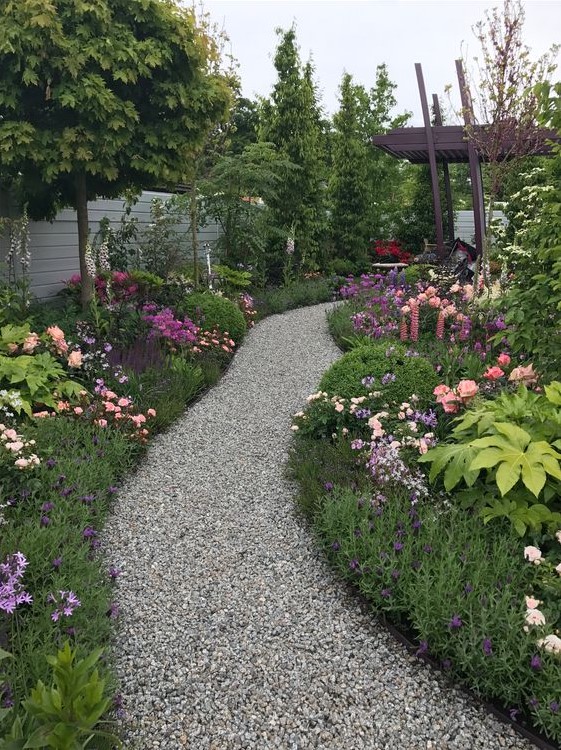 a gravel pathway lined by lush greenery and blooms looks like a path ina magical forest