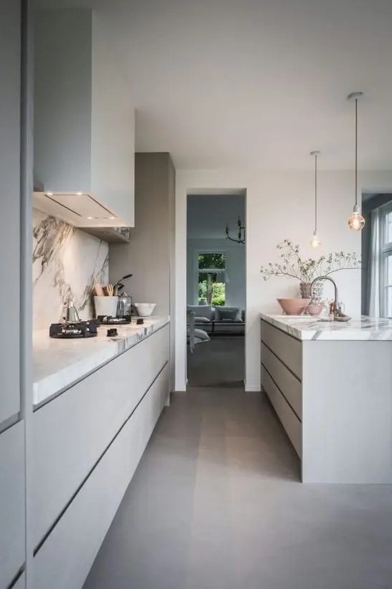 a heavenly grey contemporary kitchen with sleek cabinets and a large kitchen island, a white stone backsplash and countertops and pendant lamps