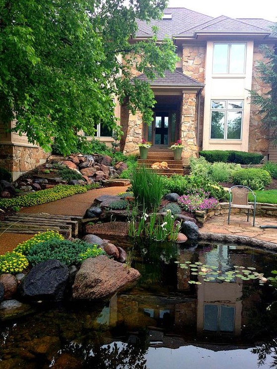 a large pond decorated with rocks with blooms and greenery makes this front yard stunning