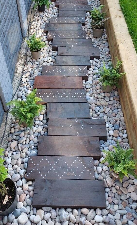 a lovely walkway with dark stained wooden steps, neutral pebbles, potted greeneyr is a gorgeous idea for a boho outdoor space