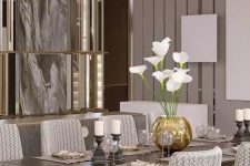 a luxurious and chic taupe dining room with a mirror accent wall, a striped wall, a chic dining table and printed chairs, candles and a lovely centerpiece