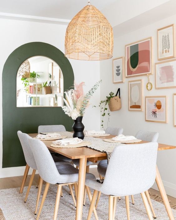 a mid century dining room with a stained table and grey chairs, a green accent wall, a pastel gallery wall
