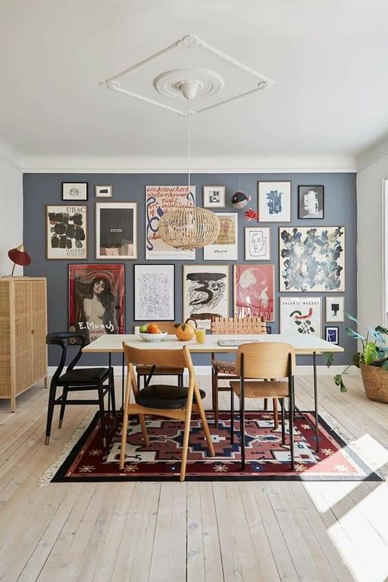 a mid-century meets boho dining room with a grey accent wall with a free form gallery wall, a simple table and mismatching chairs, a bold rug