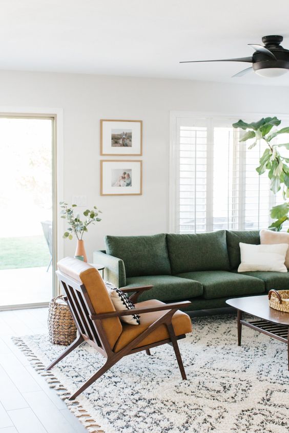 a mid century modern living room with a grene sofa, a brown leather chair, a mini gallery wall and some greenery