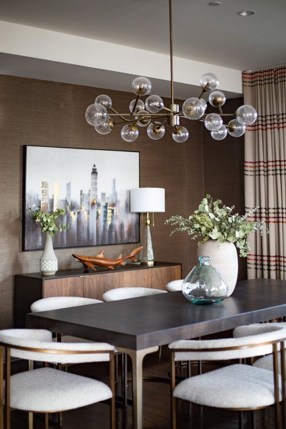 a mid-century modern taupe dining room with a credenza, a dark table and creamy chairs, a lovely chandelier