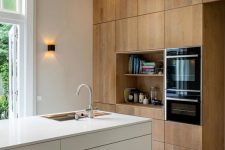 a minimalist kitchen with light-stained no hardware cabinets and a white sleek kitchen island, built-in appliances and lots of light