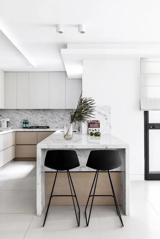 a minimalist kitchen with sleek grey and stained cabinets, a white marble backsplash and countertops, a small kitchen island with black stools
