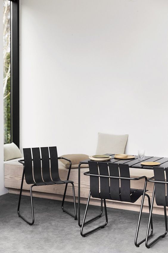 a minimalist outdoor dining space with a wood slab floating bench, a metal dining table and matching black chairs plus pillows