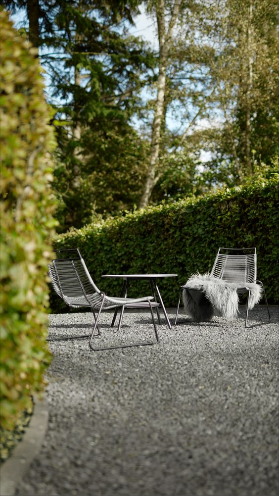 a minimalist terrace with pebbles, black metal chairs and a round table and lots of greenery around-who needs more than that