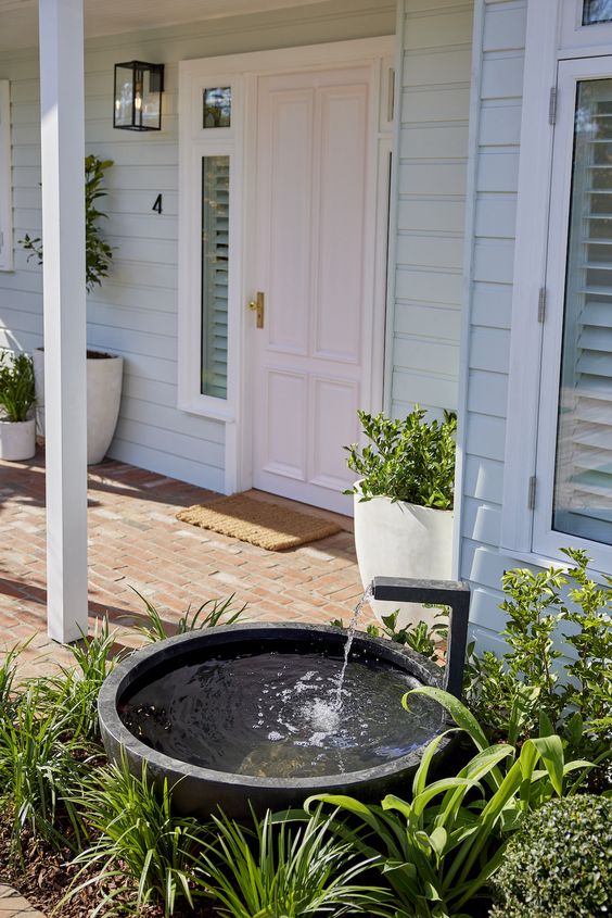 a modern entrance styled with greenery, potted plants and an ultra-modern and edgy fountain of a stone bowl and a metal faucet