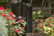 a modern fountain of large dark stones nestled in a bed of impatiens by the front door