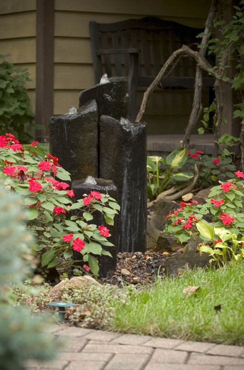 a modern fountain of large dark stones nestled in a bed of impatiens by the front door