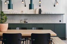 a modern kitchen with sleek no hardware cabinets, a terrazzo backsplash, a long open shelf, green pendant lamps and cool sconces, a blonde wood table and a bench, black chairs