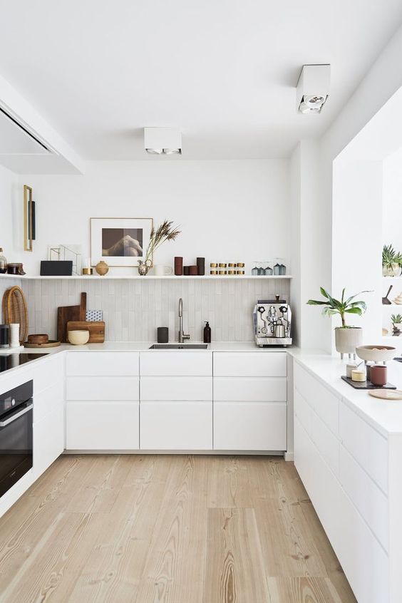 a modern white kitchen with no hardware cabinets, white stone countertops, an open shelf, some built in appliances and gold touches