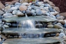 a natural looking waterfall done with large rocks and with pebbles around will bring a fresh feel to your front yard