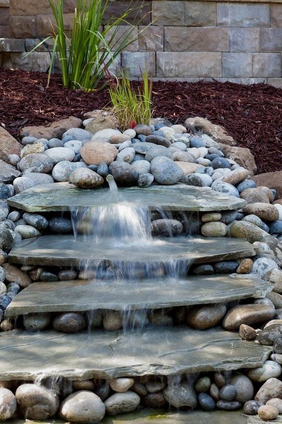 a natural looking waterfall done with large rocks and with pebbles around will bring a fresh feel to your front yard