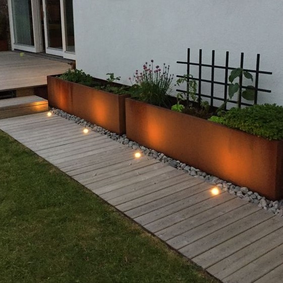 a neutral wooden garden path with a perfectly manicured lawn on one side and metal garden planters placed on pebbles on the other creates a chic modern look