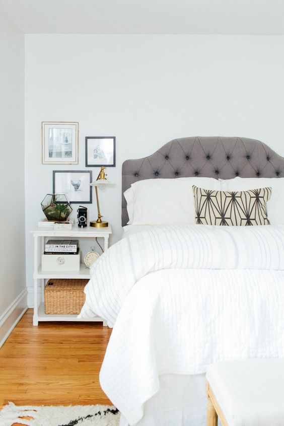 a peaceful neutral bedroom with a grey upholstered bed, a white nightstand, a gold table lamp and a mini gallery wall