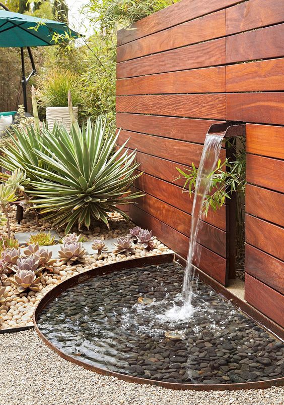 a peaceful waterfall out of a stained wall, with pebbles on the bottom and succulents growing around for a bold front yard design
