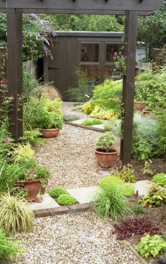 a pretty relaxed garden with greenery, blooms in pots and not only, with a gravel path and some dark wood