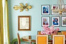 a quirky colorful dining room with mint green walls, a chic polished table and orange chairs, a statement chandelier and a grid colorful gallery wall