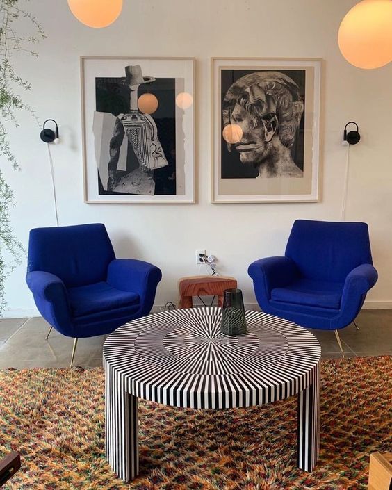 a quirky space with cobalt blue chairs, a striped round table, a colorful rug and a black and white gallery wall