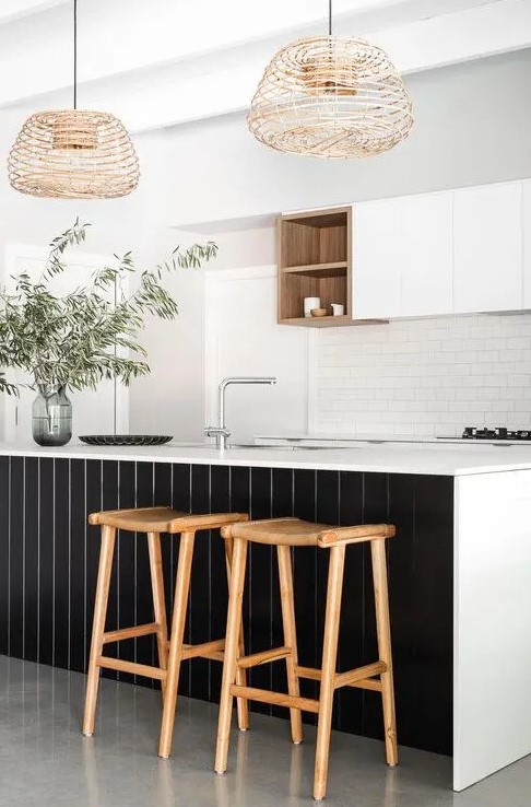 a refined contrasting kitchen with sleek white cabinets, a white subway tile backsplash, a large kitchen island with black planks, woven pendant lamps