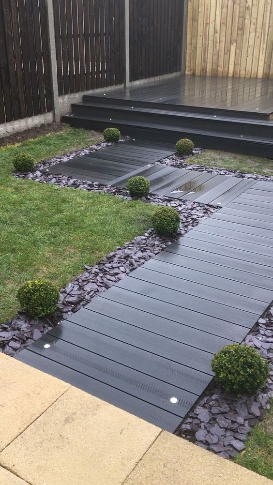 a refined dark stained wooden walkway with built in lights, rocks around, greenery along the garden path is wow a refined dark-stained wooden walkway with built-in lights, rocks around, greenery along the garden path is wow