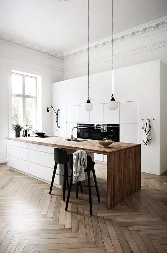 a refined minimalist kitchen with sleek white cabinets, a large kitchen island with a wooden waterfall countertop, black stools and pendant lamps