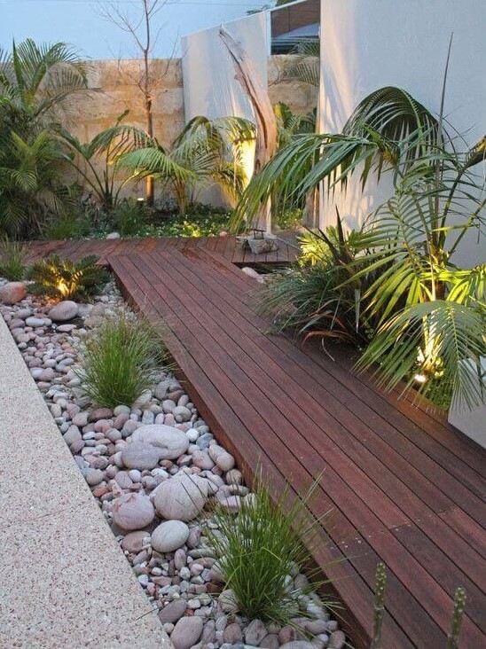 a rich-stained wooden garden path with large pebbles and rocks plus some greenery and lights around is perfect for a modern outdoor space