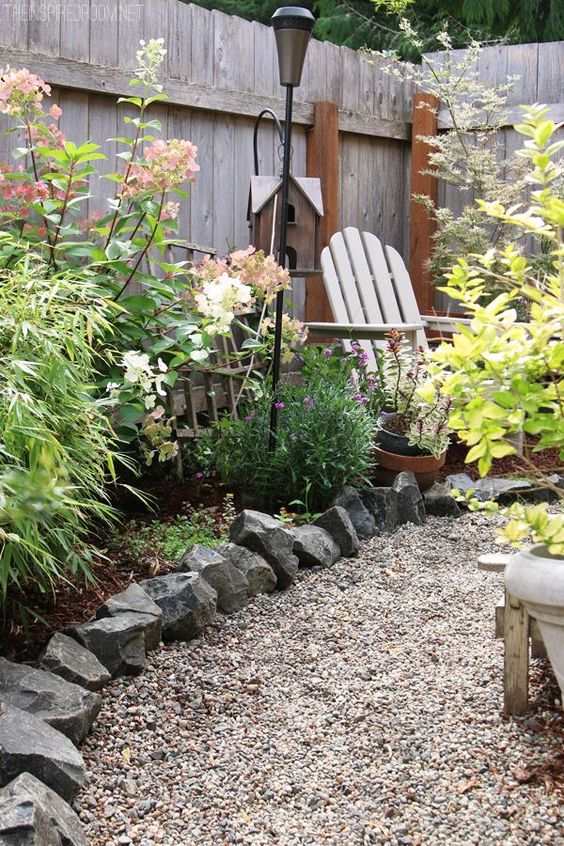 a rustic garden with blooms and colorful foliage, with gravel pathways with rock edging, some simple wooden furniture