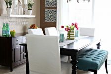 a rustic taupe dining space with a black credenza, a black dining table, a blue bench and creamy chairs, a vintage chandelier