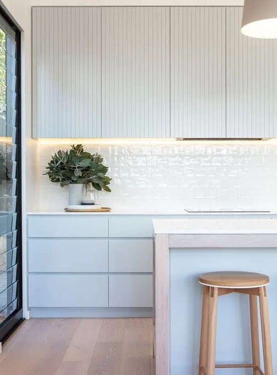 a serene contemporary kitchen with pale blue cabinets, planked and sleek ones, white glazed tiles and a matching blue kitchen island
