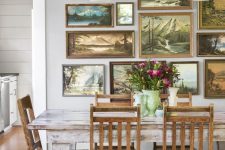 a shabby chic dining room with a whitewashed table and stained chairs, a fantastic gallery wall of gorgeous painted sceneries