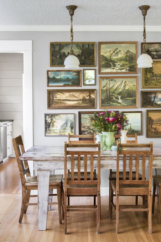 a shabby chic dining room with a whitewashed table and stained chairs, a fantastic gallery wall of gorgeous painted sceneries
