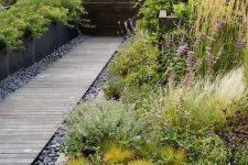 a simple and stylish weathered wood walkway with built-in lights and grey pebbles around and greenery