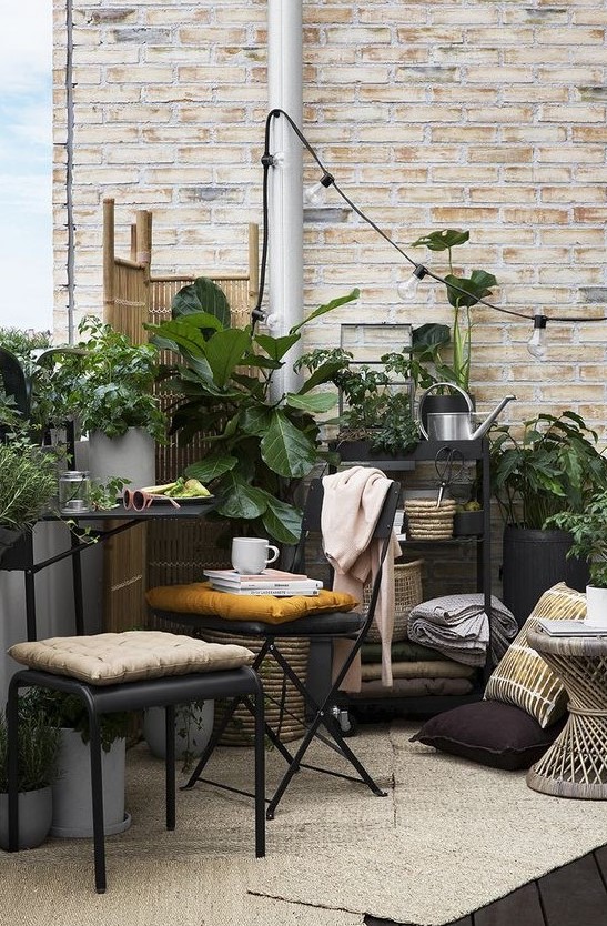 a small boho terrace with metal furniture, a wooden table, potted greenery, lights and a wooden screen