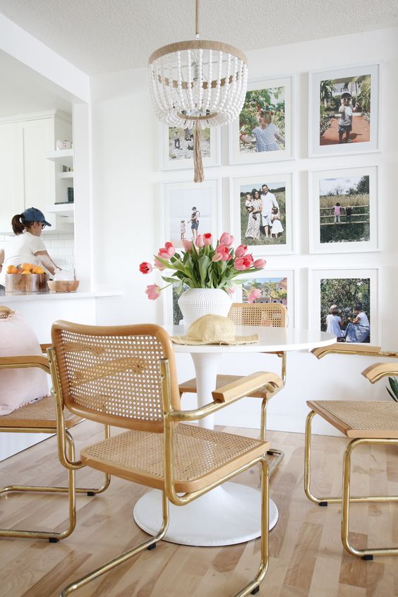a small and cozy dining space with a round table and cane chairs, a colorful grid gallery wall with family photos
