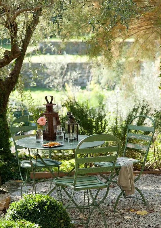 a small and cozy garden dining area wiht simple green metal furniture is located under the tree and is very inviting