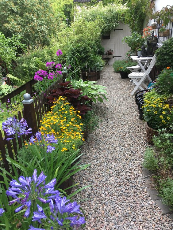 a small backyard with a gravel path, bold blooms and greenery and garden furniture is a lovely idea