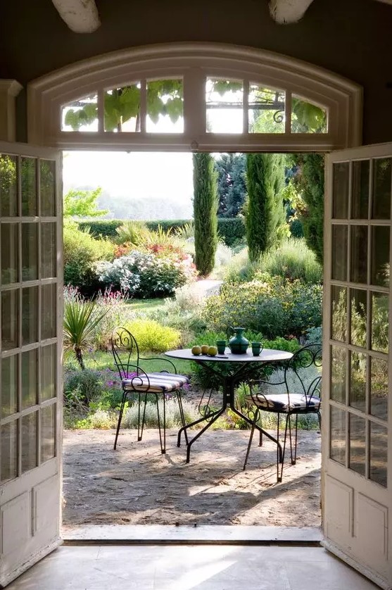 a small yet chic Provence outdoor space with a metal round table and forged chairs with striped cushions and lots of greenery and blooms around
