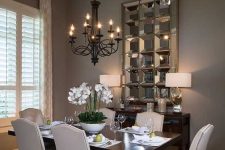 a stylish and exquisite taupe dining room with a dark-stained table and a credenza, neutral chairs, a black vintage chandelier and a mirror piece on the wall